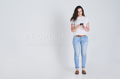 Buy stock photo Shot of young woman using her cellphone against a grey background