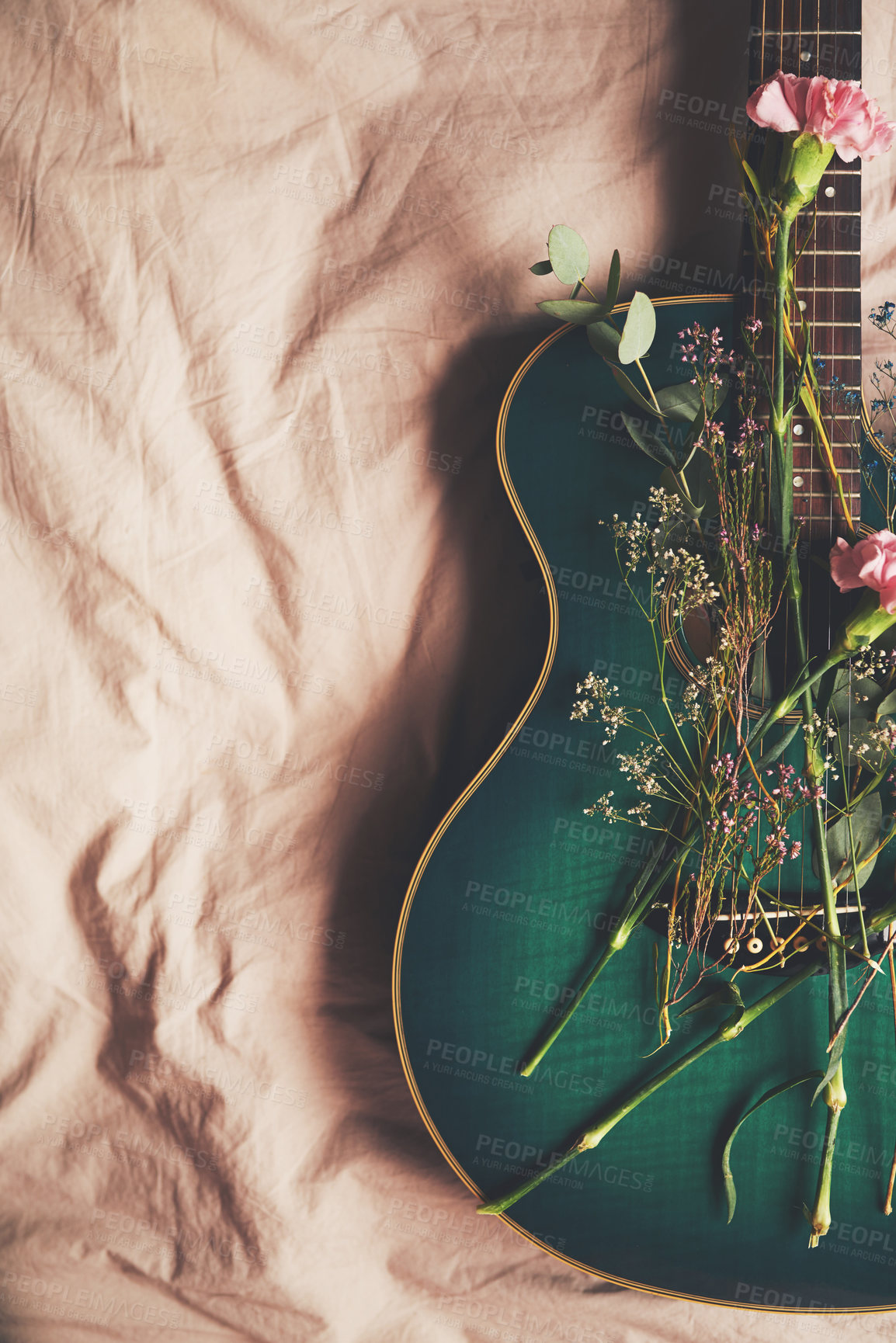 Buy stock photo High angle shot of a green guitar lying on a bed with flowers arranged on it