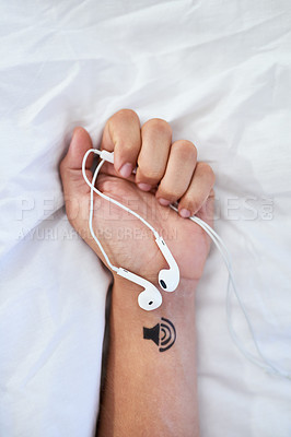 Buy stock photo Closeup shot of an unrecognizable man holding a pair of earphones with an illustration of a speaker tattooed on his wrist