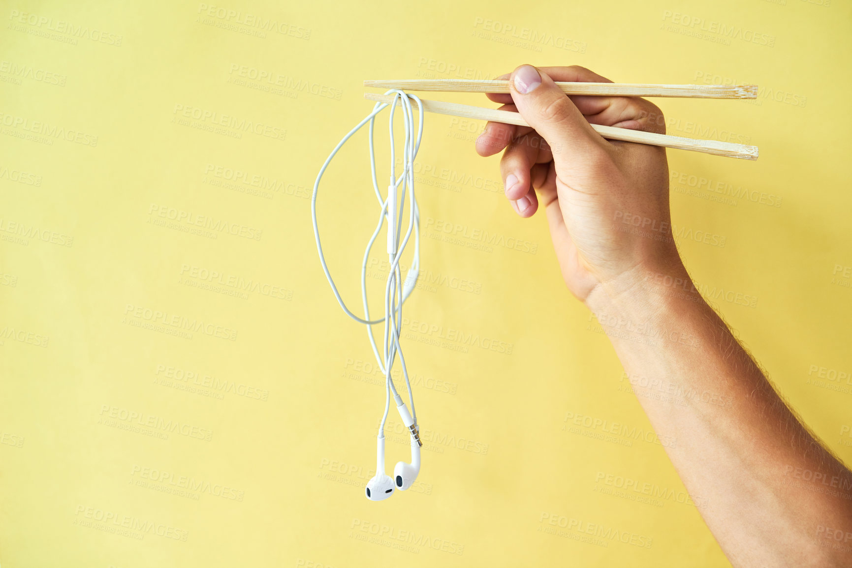 Buy stock photo Cropped studio shot of a man holding earphones wrapped around chopsticks against a yellow background