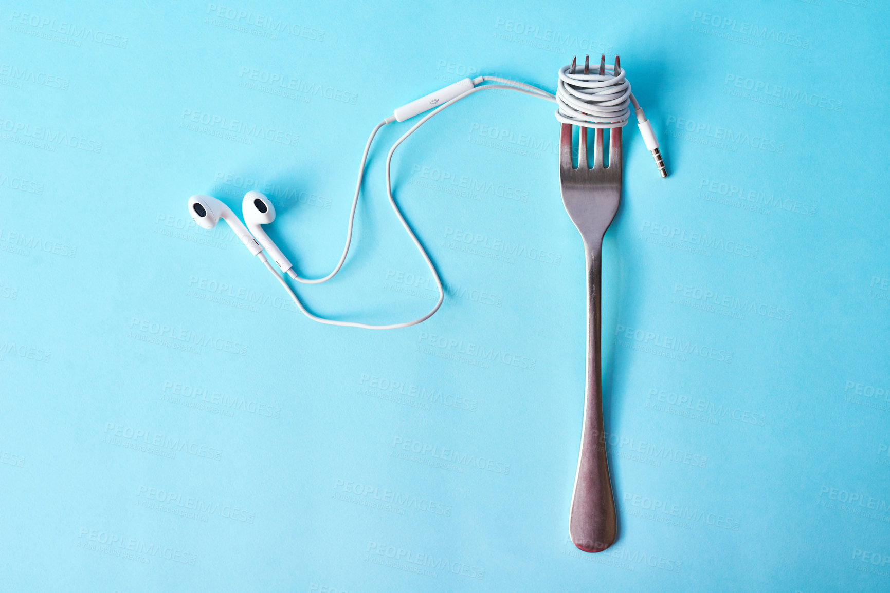 Buy stock photo Studio shot of earphones wrapped around a fork against a blue background