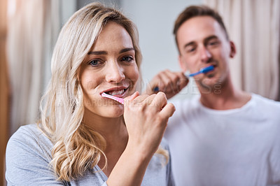 Buy stock photo Portrait of a young couple brushing their teeth together in the bathroom at home