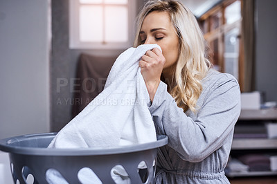 Buy stock photo Shot of a young woman smelling fresh and clean laundry at home