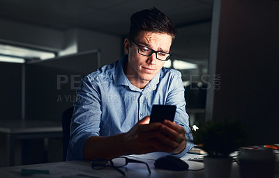 Buy stock photo Confused businessman texting on his phone at the office at night. Handsome, confident and corporate caucasian male looking at messages from coworkers while working overtime and feeling unsure 