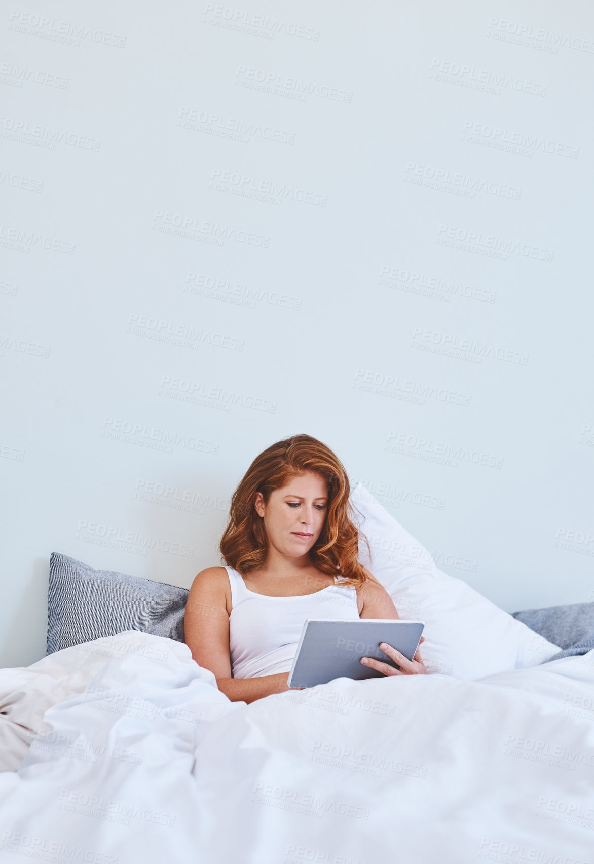 Buy stock photo Shot of a young woman using a digital tablet while relaxing in bed at home