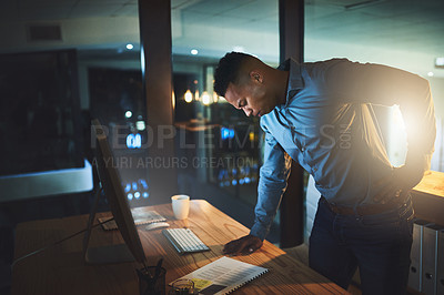 Buy stock photo Cropped shot of a handsome young businessman suffering with back pain while working late at night in a modern office