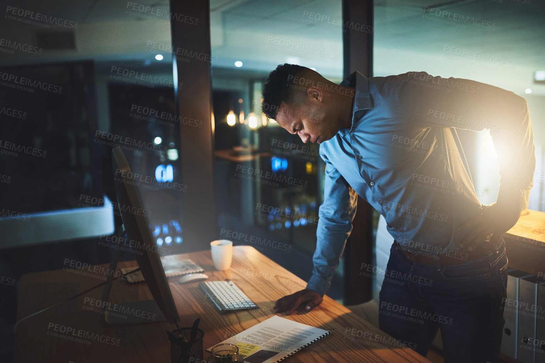 Buy stock photo Dark, office and black man at desk with back pain, stress or deadline burnout at finance agency. Overtime, startup and tired consultant at computer with muscle ache, night research and funding report