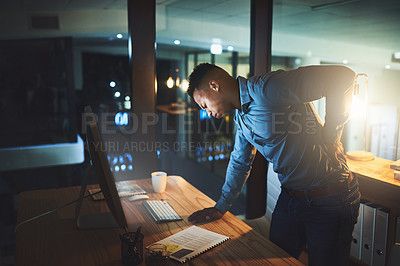 Buy stock photo Cropped shot of a handsome young businessman suffering with back pain while working late at night in a modern office