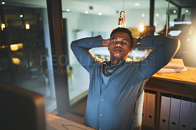Buy stock photo Cropped shot of a handsome young businessman looking relaxed while working late at night in a modern office
