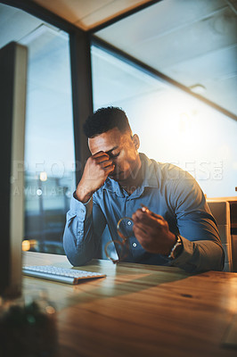 Buy stock photo Cropped shot of a handsome young businessman looking stressed while working late at night in a modern office