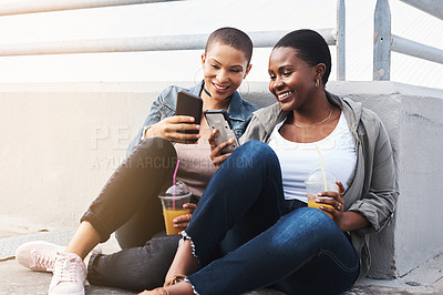 Buy stock photo Shot of two young women in the city sitting down while laughing and holding their drinks reading through text messages