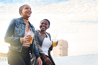 Buy stock photo Low angle shot of two young women walking in the city laughing while holding their cool drinks