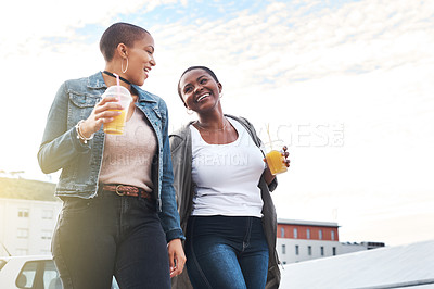 Buy stock photo Low angle shot of two young women walking in the city laughing while holding their cool drinks