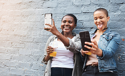 Buy stock photo Shot of two young women standing beside a building smiling and taking selfies while holding their cool drinks