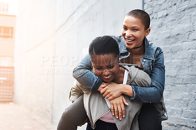 Buy stock photo Shot of a young woman carrying another on her back while laughing in the city