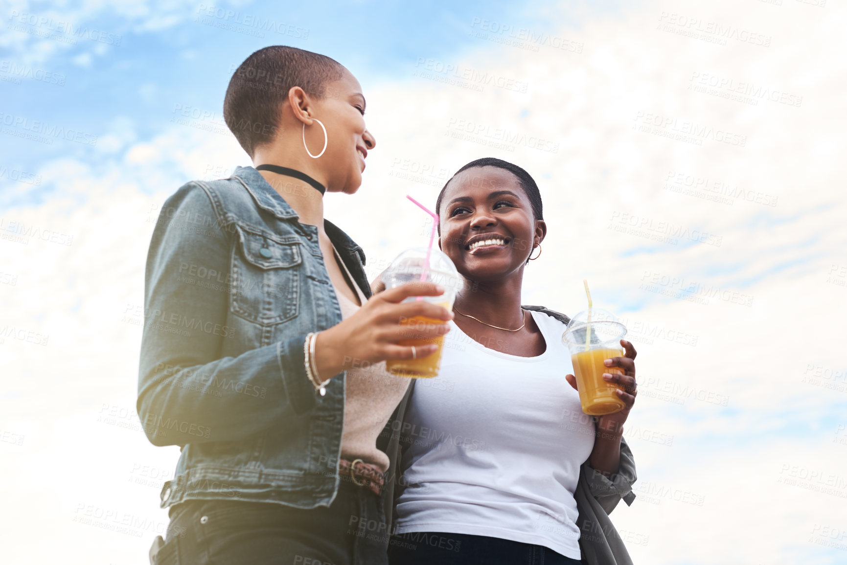 Buy stock photo Low angle shot of two young women walking in the city laughing while holding their cool drinks