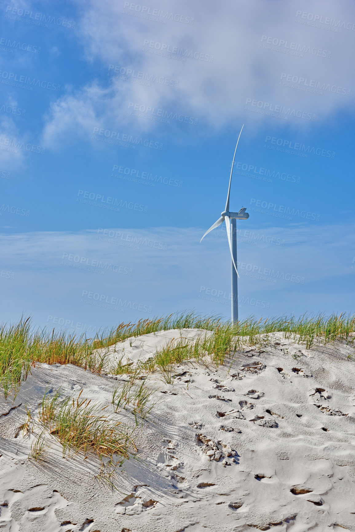 Buy stock photo One modern windmill generating renewable energy on a beach hill against a blue sky. Wind turbine making sustainable electricity by spinning propeller blades. Conceptual nature scene for eco living