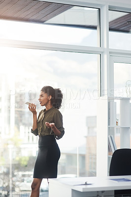Buy stock photo Shot of a young businesswoman standing in her office and busy talking on a smartphone