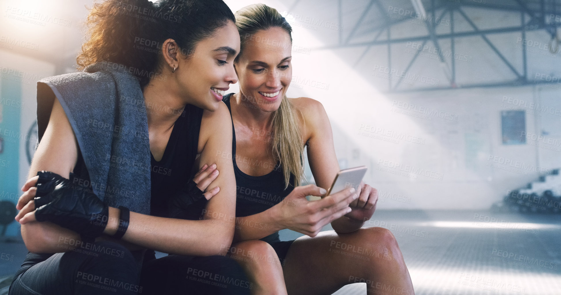 Buy stock photo Cropped shot of two attractive sportswomen in the gym sitting down and reading text messages