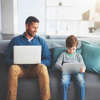 Buy stock photo Shot of a cheerful little boy and his father using a laptop and a digital tablet while being seated on a sofa at home during the day