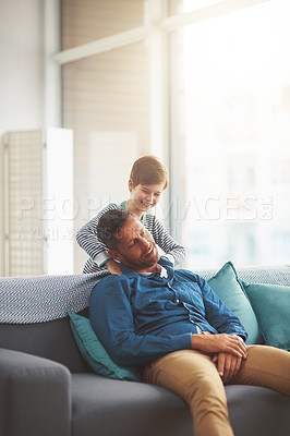 Buy stock photo Shot of a carefree little boy giving his father a massage on his shoulders while he relaxes on the sofa at home