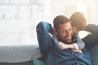 Buy stock photo Shot of a cheerful little boy giving his father a hug from behind while his father relaxes on the sofa at home