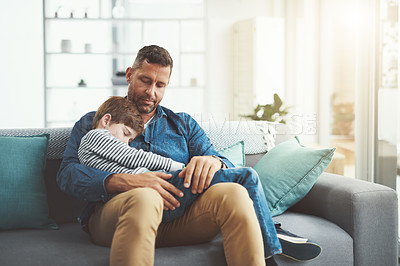 Buy stock photo Shot of a tired little boy sleeping in his father's arms while being seated on a sofa at home during the day