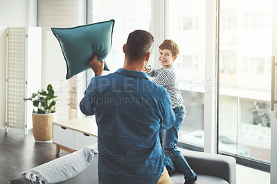 Buy stock photo Shot of a cheerful little boy and his father having a pillow fight together in the living room at home during the day