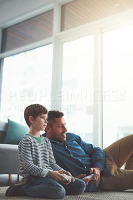 Buy stock photo Shot of a cheerful little boy and his father playing video games together on the television while being seated on the floor at home during the day