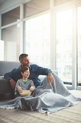 Buy stock photo Shot of a carefree young boy and his father watching a movie together while being seated on the floor at home during the day