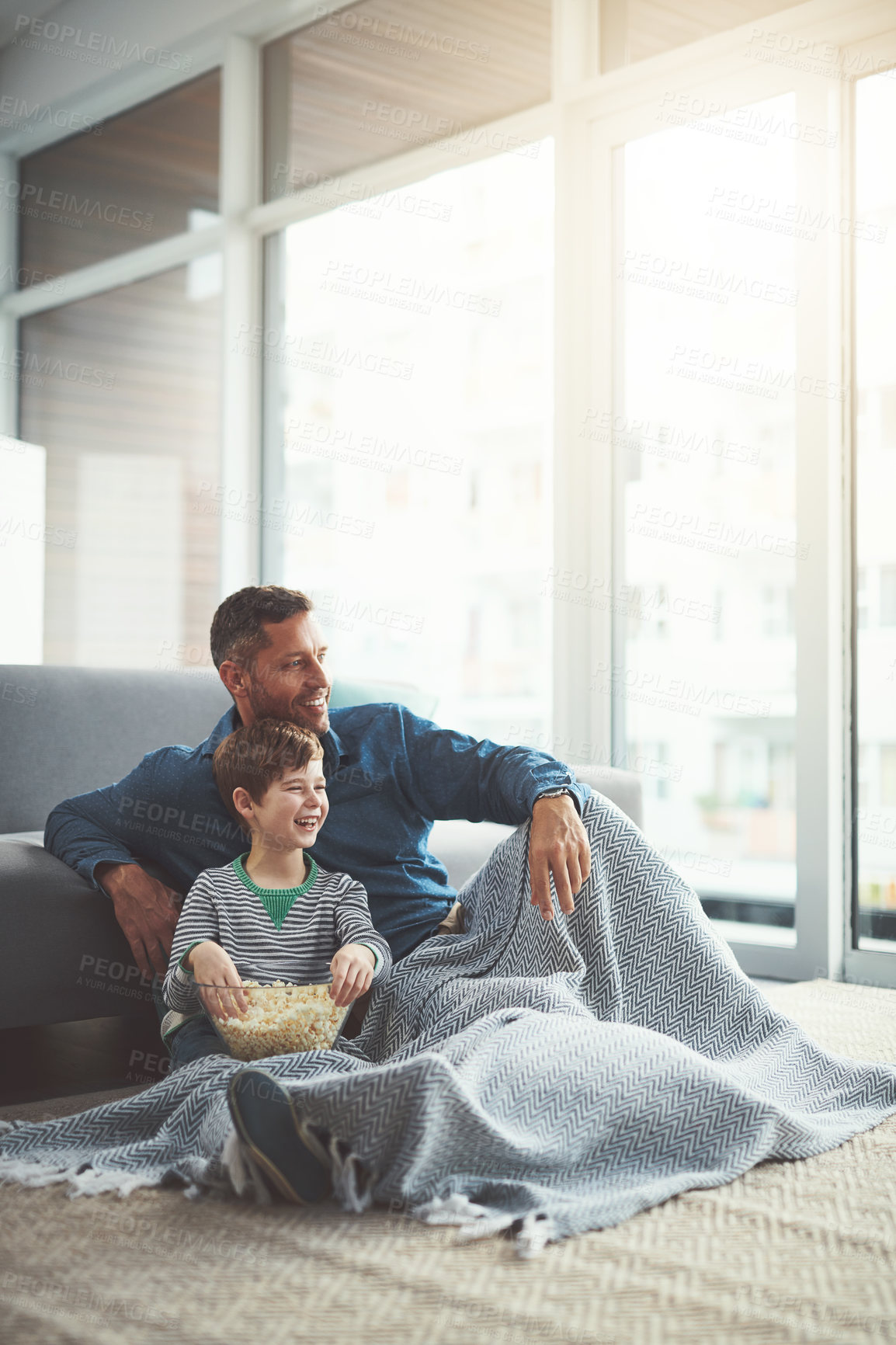 Buy stock photo Shot of a carefree young boy and his father watching a movie together while being seated on the floor at home during the day