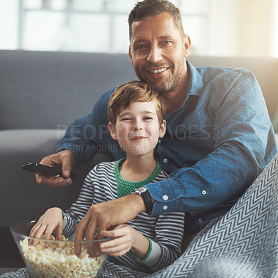 Buy stock photo Portrait of a carefree young boy and his father watching a movie together while being seated on the floor and eating popcorn at home during the day