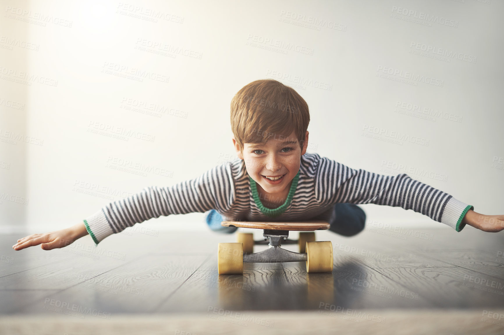 Buy stock photo Portrait of a cheerful little boy lying down on a skateboard at home during the day