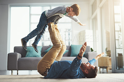 Buy stock photo Shot of a cheerful little boy playing around and being lifted by his dad with his legs in the living room at home during the day