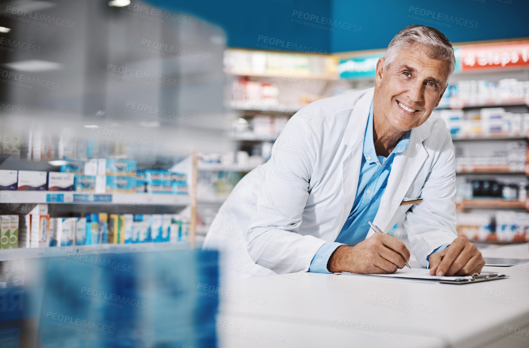 Buy stock photo Shot of a male pharmacist writing on a clipboard in a drugstore