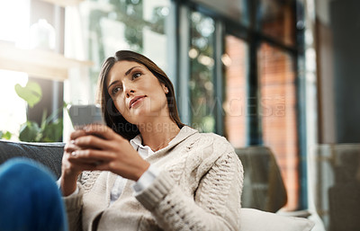 Buy stock photo Shot of an attractive young woman looking thoughtful and sending text messages while relaxing on her sofa at home