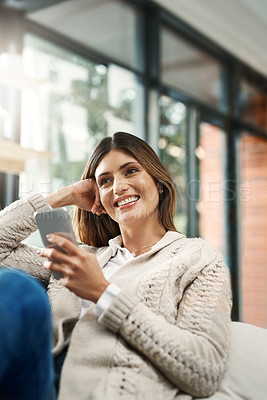 Buy stock photo Shot of an attractive young woman looking thoughtful and sending text messages while relaxing on her sofa at home