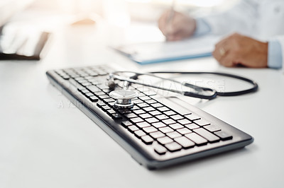 Buy stock photo Cropped shot of a keyboard with a stethoscope on it while an unrecognizable man writes on a form in the background