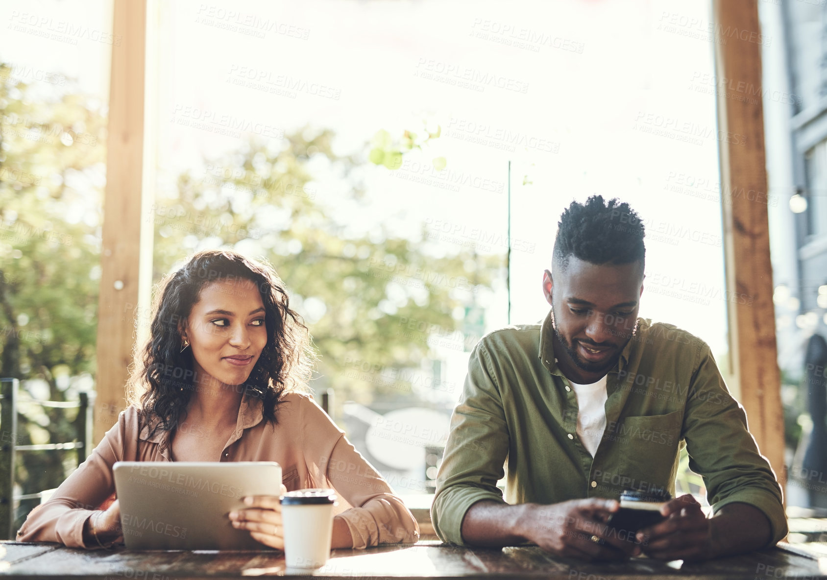 Buy stock photo Shot of two young people using their wireless devices in a coffee shop