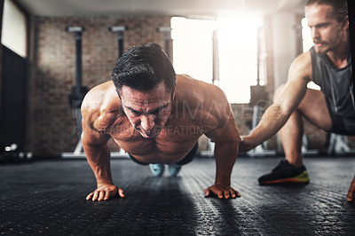 Buy stock photo Shot of a muscular young man working out with his fitness trainer in a gym