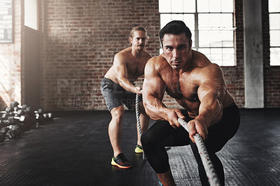 Buy stock photo Shot of two muscular young men pulling on a rope in a gym