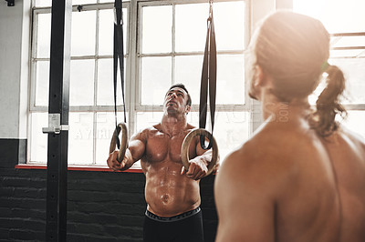 Buy stock photo Shot of two young men exercising with gymnastic rings in a gym