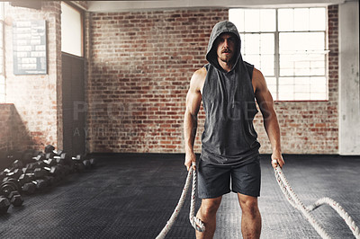 Buy stock photo Shot of a muscular young man working out with battle ropes in a gym