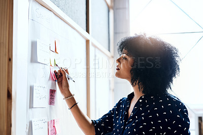 Buy stock photo Shot of a young female designer doing some planning and using sticky notes on a white board in the office