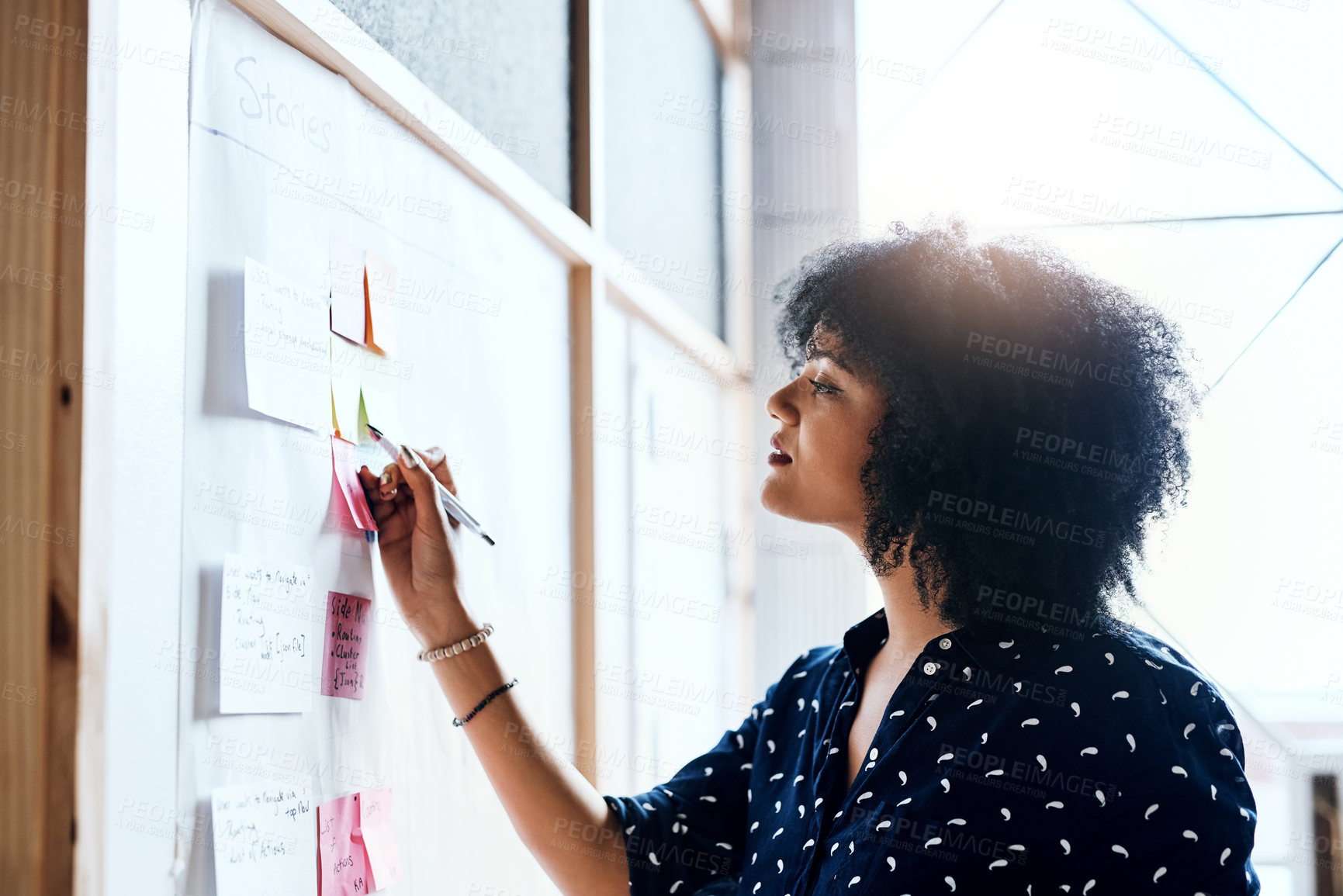 Buy stock photo Shot of a young female designer doing some planning and using sticky notes on a white board in the office