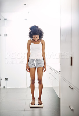 Buy stock photo Full length shot of an attractive young woman weighing herself on a scale in the bathroom at home