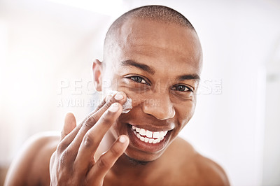 Buy stock photo Portrait of a handsome young man applying moisturizer to his face in the bathroom at home