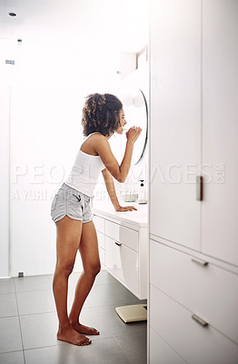 Buy stock photo Full length shot of a young woman brushing her teeth while standing in her bathroom at home