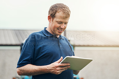 Buy stock photo Shot of a cheerful young male farmer holding a digital tablet while standing outside on his land