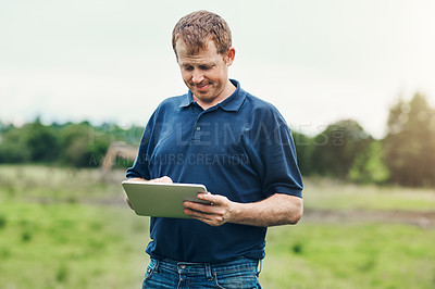 Buy stock photo Shot of a cheerful young male farmer holding a digital tablet while standing outside on his land